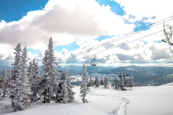 Winterberglandschaft. Im Vordergrund Fichte und Seilbahn vor dem Hintergrund von Berggipfeln, dicken Wolken und blauem Himmel. russlandscheregesch. — Stockfoto