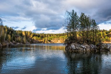 Sonbahar manzarası. Ormanla çevrili bir gölün ortasında ağaçlar olan taş ada..