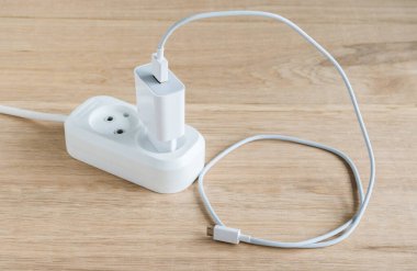 Elektrik hattına bağlı akıllı telefonlar için USB kablosu olan şarj aleti. Ahşap masa arkaplanı.
