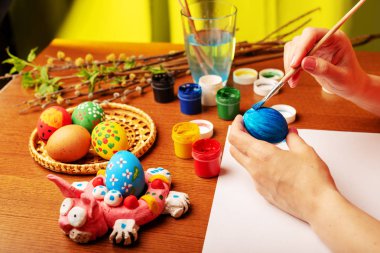 Sanatçı Paskalya dini öğeleri boyar. Boyama için hazırlanan tavuk, sepete biridir. Dalları Söğüt ve çiçeklenme ile Lila yeşil yaprakları. Boya fırçaları ve bir bardak su ile bir kavanoza. Eller yakın çekim