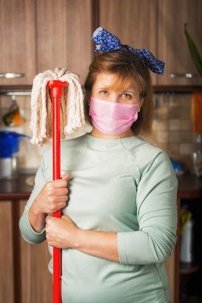 Person with a mop in hands and detergent. Protective medical mask and the spray for disinfecting. Purity and an order in the territory of kitchen. Healthy food. Fight against a virus and microbes.