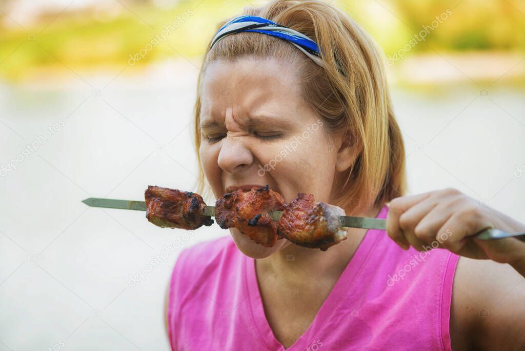 A person greedily eats shish kebab. The skewer is held in the hands. Well-grilled pieces of pork and lamb.