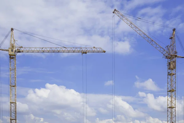 Copy space between two construction cranes against blue cloudy sky