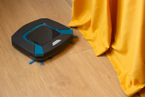Robotic vacuum cleaner on wooden floor in cozy living room with yellow curtains. Home cleaning concept