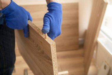 Profesyonel marangoz ustası mobilyaları mavi eldivenlerle monte ediyor.