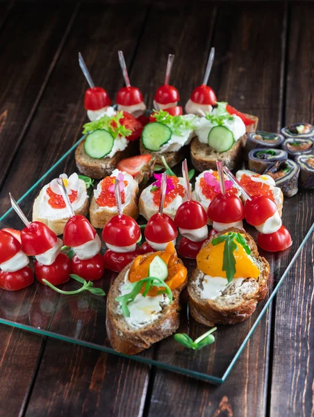 Imbisstablett auf holzigem Hintergrund: Brötchen, Canapes, Semmeln, gefüllte Tomaten, Sandwich mit Kaviar. Ansicht von oben — Stockfoto