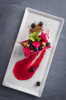 Beyaz, kırmızı parlak dondurma yaban mersini, böğürtlen ve karamel beyaz bir tabakta. Yaratıcı servis yemekleri. Üst görünüm, gri arka plan