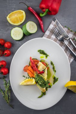 Limon, havuç ve sos salsa verde ile Fırında Halibut balık biftek. Beyaz tabak, kekik, kaşık, gri arka plan üzerinde çatal. Üstte görüntü