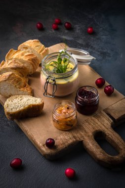 Ahşap doğrama tahtası üzerinde kızılcık ve ekmek dilimleri ile ördek karaciğer pate Cam kavanoz. Koyu doku arka planı. Metin için alan