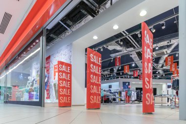 Sezon satış, black friday ve alışveriş konsepti. Kırmızı satış işareti ile giyim mağazası girişinde anti-hırsızlık sensörü kapıları. Arka planda kıyafetler. Minsk, Beyaz Rusya - Ağustos, 2019