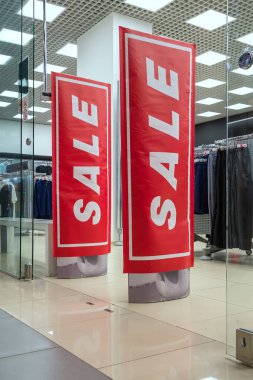 Sezon satış, black friday ve alışveriş konsepti. Kırmızı satış işareti ile giyim mağazası girişinde anti-hırsızlık sensörü kapıları. Arka planda giysiler.