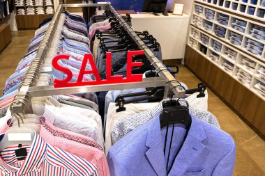 Mağazadaki erkek gömlek ve ceketler bölümünde satış tabelası. Bir perakende dükkanında askıları renkli giysiler. Sezon satış, black friday, moda ve alışveriş konsepti