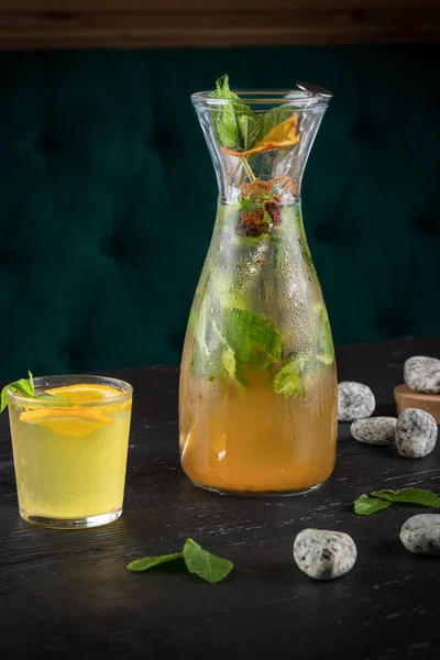 Lemonade drink of soda water, lemon and mint leaves in jar and glass on the black background