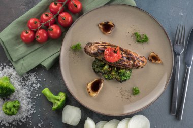 Izgara domuz bonfile, pişmiş brokoli, kiraz domates, soğan confiture üzerinde yakından görünümü. Gri arka plan, kaşık ve çatal