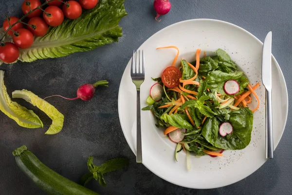 Salade d'été avec vinaigrette au sésame à la menthe, radis, tomates cerises, carotte, feuilles de laitue. Fond gris, cuillère et une fourchette — Photo