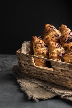 Arka plan olarak gri bir masa üzerinde hasır sepet içinde lezzetli ve taze Fransız kruvasan