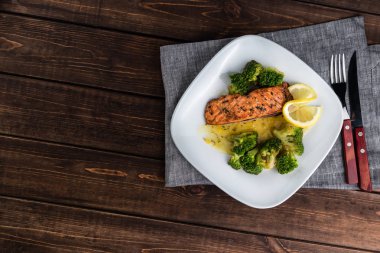 Brokoli ve kireç ile beyaz bir tabak ta ızgara alabalık biftek. Ahşap arka planda çatal bıçak takımı. Metin için boş alan