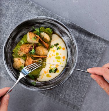 Kadınların elleri kaşık ve çatal tutuyor. Gri bir masa örtüsü üzerinde Gri kil plaka içinde yumuşak bezelye ve Beurre Blanc Sos ile tarak