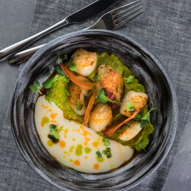 Yumuşak bezelye ve Beurre Blanc Soslu tarak. Gri kil plaka, kaşık, gri bir masa örtüsü üzerinde çatal