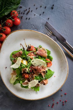 Burrata, parma ve kiraz domates ile Salata confit. Kaşık ve gri arka plan üzerinde bir çatal