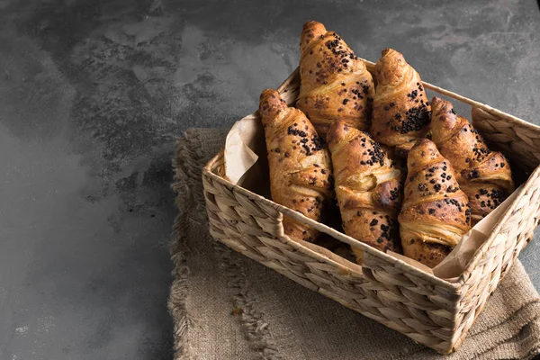 Вкусные и свежие французские круассаны в плетеной корзине закрываются на сером столе в качестве фона. Свободное место для текста — стоковое фото