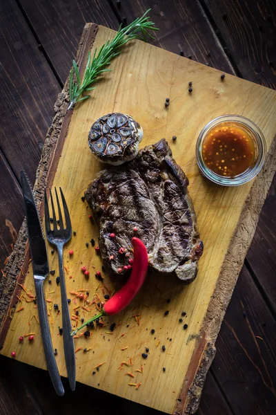 Grillezett marha steak Bourbon mártással, fa vágódeszka. Piros chili paprika és kakukkfű a barna fa háttérben. Vertikális fénykép. — Stock Fotó