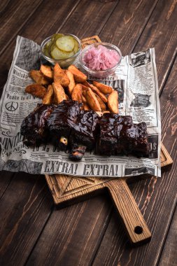 Minsk, Beyaz Rusya - Ağustos, 2019 Pişmiş patates ve salatalık turşusu ile ayarlanmış Barbekü Domuz kaburga kahverengi ahşap arka plan üzerinde yalan ahşap arka plan kurulu gazete ile hizmet