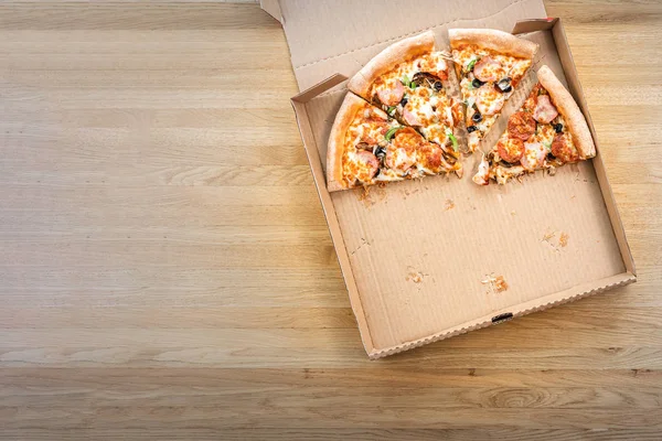 Restoranda ahşap masaüzerinde karton kutuda dilimlenmiş pizza yarısı. Metin için üst görünüm ve kopyalama alanı