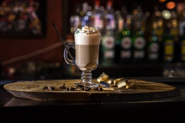 Ahşap bar sayacı üzerinde şeffaf cam latte macchiato kahve. Deodaklanmış arka plan ve fotokopi alanı ile restoran şişeleri