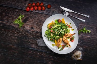 Karides, domates, arugula, ahşap koyu arka plan üst görünümünde turuncu ile taze salata tabağı. Rustik tarzda sağlıklı gıda konsepti