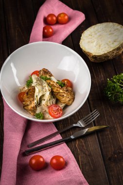 Kereviz kökü, tavuk filetosu, beyaz tabakta kiraz domates salatası. Pembe masa örtüsü, kaşık ve çatal kahverengi bir arka plan üzerinde yalan