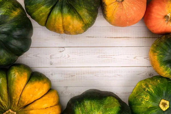 Quadro feito de abóboras verdes, amarelas, vermelhas e laranja sobre fundo de madeira branca. Conceito criativo de outono. Flat lay, vista superior, espaço de cópia — Fotografia de Stock