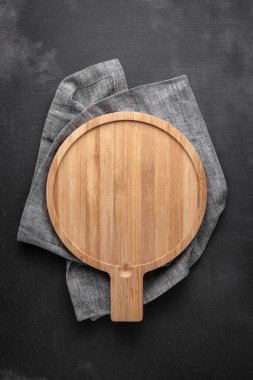 Siyah ve gri arkaplanının ortasında masa örtüsü olan ahşap kesme tahtası. Metnin için boş alan, üst görünüm