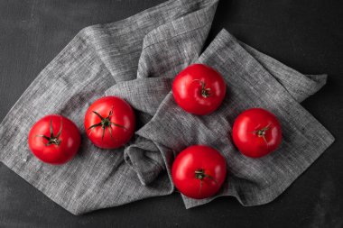 Masa örtüsünün üzerinde bir grup kırmızı ve olgun domates. Koyu siyah ve gri desenli arka plan. Reklam için şablon, üst görünüm