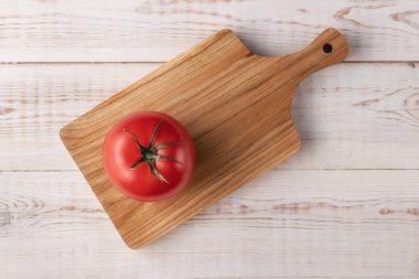 Tahta kesme tahtasının ortasında kırmızı ve taze bir domates. Beyaz desenli arka plan. Sağlıklı vejetaryen organik gıda konsepti.