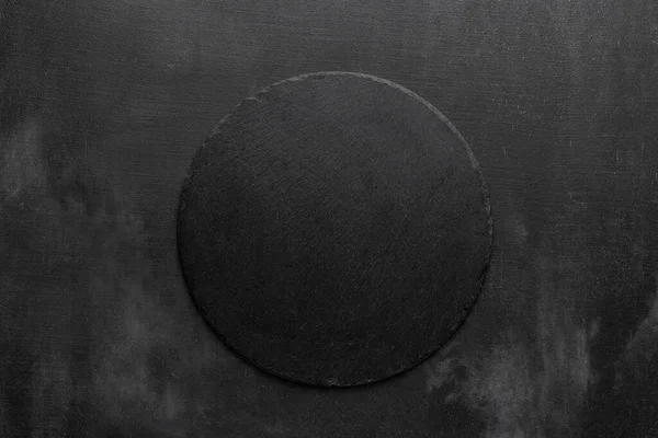 Round black slate stone plate in the middle of a dark grunge scratched background. template for menu in restaurant. free space for your text