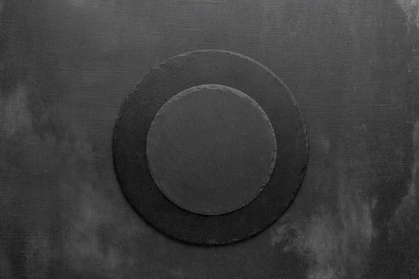 two round black slate stone plates in the middle of a dark grunge scratched background. template for menu in restaurant. free space for your text