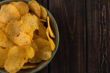 Yakın plan yeşil tabak üzerinde lezzetli kıvrımlı altın patates cipsi kızartılmış ve kahverengi ahşap arka planda tuzlanmış fotokopi alanı, üst görünüm