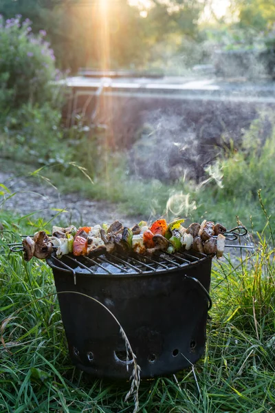 Sebze şişleri dumanlı barbeküde kanal kenarındaki küçük teknenin yanında yazın alacakaranlıkta.