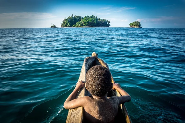 back view of little african boy in canoe floating among ocean to island