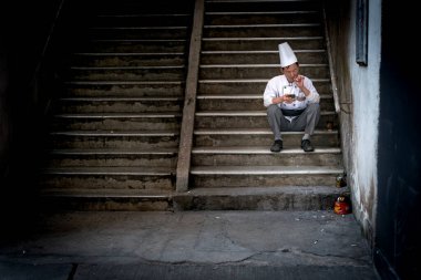 Hong Kong-05.30.2020: Beyaz şapkalı restoran şefi merdivenlerde oturup sigara içerek rahatlıyor