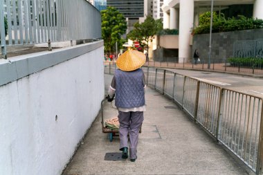 Hong Kong sokaklarında geleneksel bambu şapkayla yürüyen temizlikçi.