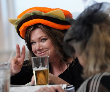 A woman in a very colorful hat enjoys a beer at the bar during Ladies Day at Arizona Downs, Prescott Valley, Arizona on August 10, 2019. clipart