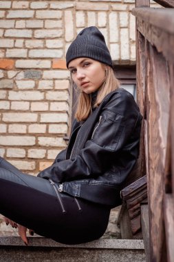 şık güzel kız kadın sarışın poz siyah bir şapka, siyah deri ceket ve pantolon, yüksek botlar şehir sokak tarzında yürür. Portre. adımda oturan.