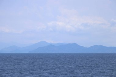 Arka plan olarak dağlar ve gökyüzü ile mavi deniz.