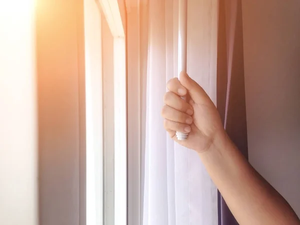 Woman\'s hand holding a curtain holder to close the curtains to protect the sunlight. Slide the curtain to reduce the light into the house.