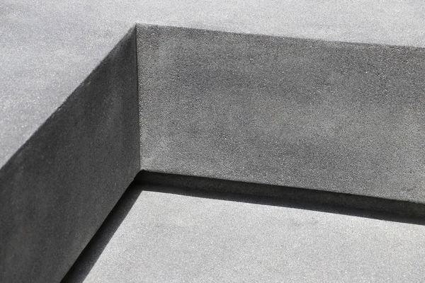 A seat in the park that looks like a right angle. The seat is made of cement.