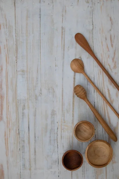 Eco-friendly wooden bowls, spoons and honey stick on wooden table background. Environmentally friendly tableware flat lay with copy space.