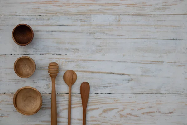 Eco-friendly wooden bowls, spoons and honey stick on wooden table background. Environmentally friendly tableware flat lay with copy space.