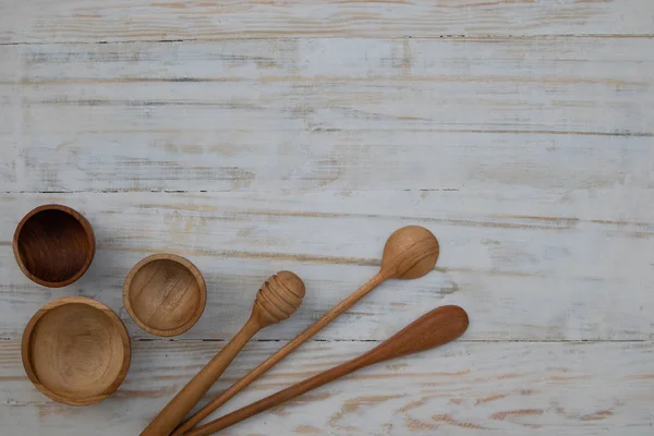 Eco-friendly wooden bowls, spoons and honey stick on wooden table background. Environmentally friendly kitchen utensil flat lay with copy space.
